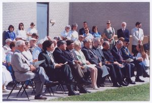 La cérémonie de la première pelletée. On y voit à la première rangée de gauche à droite, l’abbé Georges Damphousse, Dan Vandal, Ron Duhamel, le lieutenant-gouverneur Yvon Dumont, la ministre Rosemary Vodrey, Neil Gaudry, Henri Bouvier, Mgr Roland Bélanger, Alfred Monnin, et l’aide de camp du lieutenant-gouverneur. On y voit aussi debout au coin à droite Peter Stechishin et George Cibinel.Archives de la SHSB, Fonds La Liberté, SHSB 99915